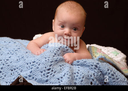 Fünf Monate altes Baby, stricken decken, mit einem lustigen Gesichtsausdruck auflegen. Stockfoto