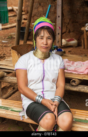 Die jungen Burmesischen Karen lange Hals Frau mit Halsring, eine burmesische Flüchtlinge, die außerhalb einer Lehmhütte in Padong Karen Dorf sitzen, Chiang Rai, Thailand Stockfoto