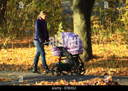 Frau mit Baby im Perambulator im Herbst Park spazieren Stockfoto