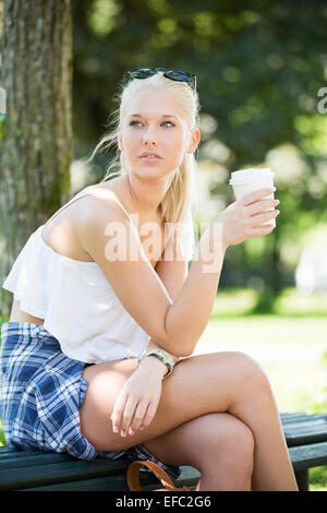 Casual Mädchen sitzt auf einer Bank und trinkt Kaffee Stockfoto