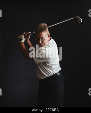Reifer Mann Golfer tragen ein weißes Hemd und He Übung eine Schaukel - Studio gedreht, schwarzer Hintergrund Stockfoto