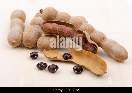 Getrocknete Tamarinde Früchte mit Samen auf Holz. Eine offene Hülse mit Fruchtfleisch im Inneren der Schale. Tamarindus Indica. Stockfoto