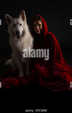 Frau trägt eine rote Haube posiert im Studio mit ihrem Hund Stockfoto