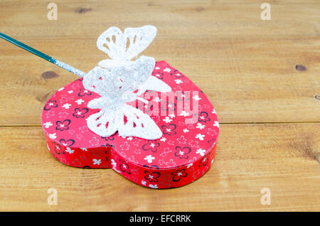 Herzförmige Box und ein Schmetterling geformt Zauberstab auf einem Holztisch Stockfoto