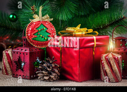Handgemachte Weihnachtskugel aus Filz in der Nähe der Weihnachtsbaum, rotes Feld, Laterne, Kegel und Kerze Stockfoto