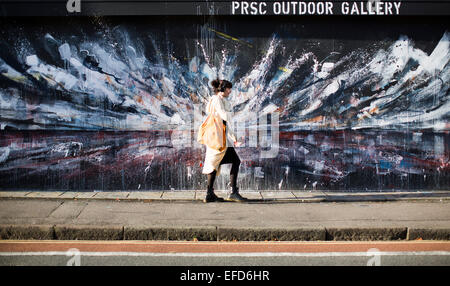 Eine Frau geht vorbei an einem Stück von urban street Art und Graffiti an der Seite eines Gebäudes in Stokes Croft, Bristol. Stockfoto