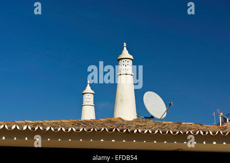 Zwei weiße Schornsteine vor einem tiefblauen Himmel in Olhos de Agua, Portugal. Die Terrakottafliesen Dach und eine Satellitenschüssel sind zu sehen. Stockfoto