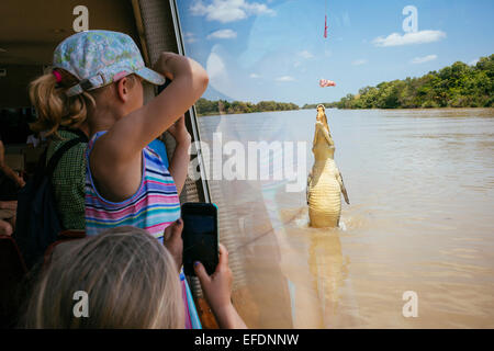 Ein junges Mädchen schaut ein springender Krokodil durch das Fenster eines Kreuzfahrt-Schiffes am Adelaide River, Northern Territory, Australien Stockfoto