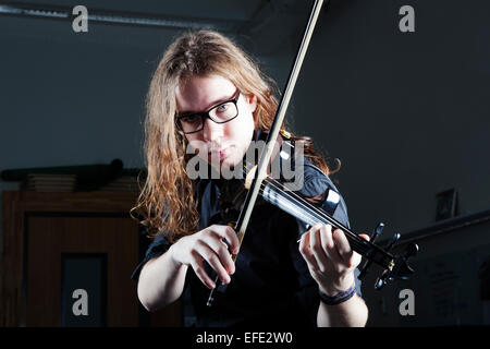 junger Mann mit langen Haaren und Brille spielt e-Geige mit grelles Licht Stockfoto