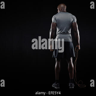 Heckansicht des muskulösen Mann stehend mit Seilspringen auf schwarzem Hintergrund. Studioaufnahme von Fitness-Modell halten skipping Rope loo Stockfoto