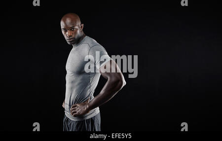 Porträt von hübscher junger muskulöser Mann posiert vor schwarzem Hintergrund. Afrikanische männlichen Fitness-Modell-Blick in die Kamera mit seinem h