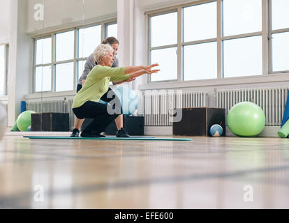 Ältere Frau Übung mit ihrem persönlichen Trainer im Fitness-Studio. Gymnastikausbilder ältere Frau in ihr Training zu unterstützen. Stockfoto