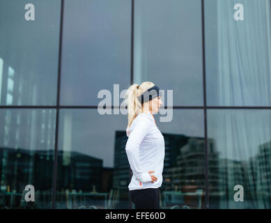 Seitlicher Blick auf eine sportliche junge Frau bereit für ihre outdoor-Training-Session. Fitness-Frau stehend im Freien mit Hände auf den Hüften. Stockfoto