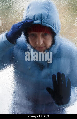 Eine Frau trägt einen dicken warmen Mantel außerhalb beim Schauen durch ein Fenster Glas Milchglas Tür, die in der Kälte zu kommen. England Großbritannien Großbritannien Stockfoto