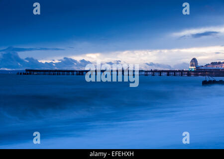 Hastings Strandpromenade und Pier. Wellen auf den Strand bei Sonnenuntergang. während die Lichter der Stadt funkeln im Hintergrund. Stockfoto