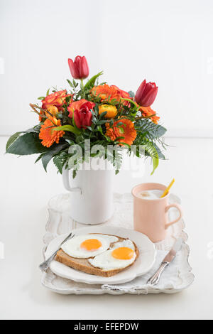 Frühstück mit Spiegeleiern, Cappuccino und einen Blumenstrauß auf einem Tablett Stockfoto