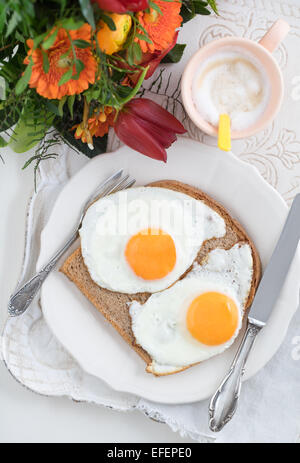 Frühstück mit Spiegeleiern, Cappuccino und einen Blumenstrauß auf einem Tablett Stockfoto