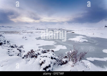 Eine gefrorene man Na Stainge auf Rannoch Moor. Die schwarzen Berg Hügel und Meall ein "Bhùiridh in der Ferne zu sehen. Stockfoto