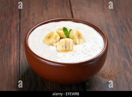 Haferflocken-Porridge mit Bananen Scheiben in Keramikschale auf Holztisch, Nahaufnahme Stockfoto