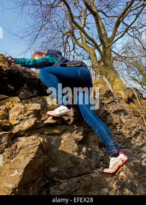 Zwölf Jahre altes Kind in Blue Jeans und Turnschuhe Klettern auf Felsen mit einem Baum und blauer Himmel im Hintergrund Stockfoto