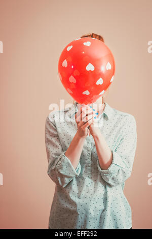 Junge Frau verbirgt ihr Gesicht hinter einem Ballon mit Herzen. Retro-Farben Stockfoto