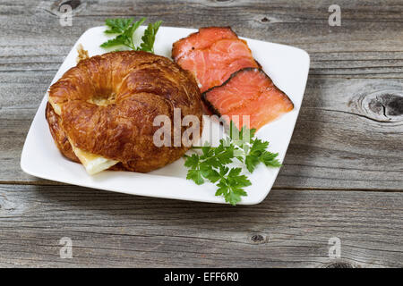 Nahaufnahme von Frühstück mit frisch gebackenen Croissants, mit Ei, kalt geräucherter Lachs und Petersilie auf Seite auf rustikalem Holzbrett Stockfoto