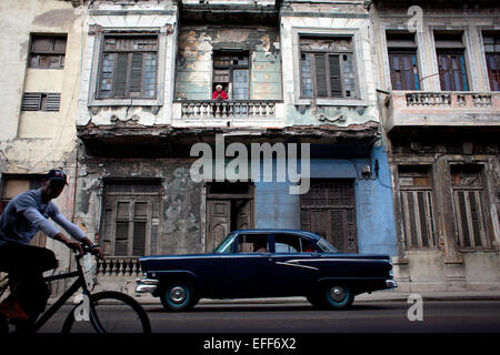 Havanna, Kuba. 28. Januar 2015. Eine Frau steht auf dem Balkon ein verfallenes Haus über eine Weitergabe von Straßenkreuzer aus den 1950er Jahren in der Innenstadt von Havanna, Kuba, 28. Januar 2015. Oldtimer aus den 1940er und 1950er Jahren sind nach wie vor eine gemeinsame Szene und Bestandteil der täglichen Citycape von Havanna. Foto: Lisette Poole/Dpa/Alamy Live News Stockfoto