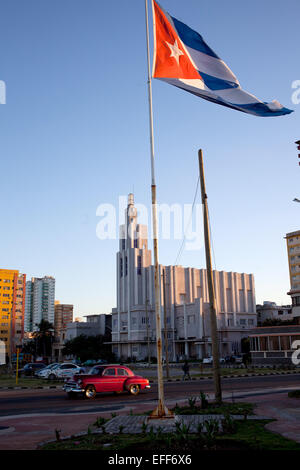 Havanna, Kuba. 28. Januar 2015. Ein Oldtimer Straßenkreuzer aus den 1950er Jahren fährt vorbei an einem Mast mit der kubanischen Nationalflagge wiegen sich im Wind in Havanna, Kuba, 28. Januar 2015. Oldtimer aus den 1940er und 1950er Jahren sind nach wie vor eine gemeinsame Szene und Bestandteil der täglichen Citycape von Havanna. Das Gebäude in den Rücken über den Platz ist die sogenannte "Casa de Las Americas" (House of the Americas), ein Kulturinstitut gegründet 1959, die Facilitrating kulturellen Austausch zwischen den Ländern in Lateinamerika, der Karibik und dem Rest der Welt angestrebt wurde. Foto: Lisette Poole/Dpa/Alamy Live News Stockfoto