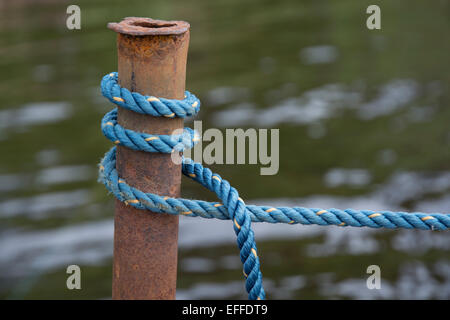 Blaues Boot Knoten Seil um rostige Pol am Wasser gebunden. Stockfoto