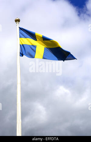 Schwedische Flagge in blau mit gelben Kreuz gegen bewölktem Himmel. Stockfoto