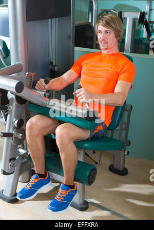 Fitness-Studio sitzt Bein Curl Maschine Übung blonden Mann im innen- Stockfoto