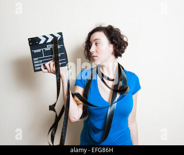 Junge hübsche Frau mit blauen lässigen t-Shirts und Filmstreifen um Hals hält und betrachten Film Klöppel auf weißen Zeitmessung Stockfoto