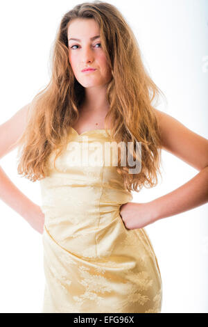 Zuversichtlich durchsetzungsfähig vierzehn 14 Jahre alten Mädchens mit langen braunen Haaren, posiert in einem Studio mit dem Gold goldene Kleid in ihre Hände auf ihre Hüften stehen nach vorn UK Stockfoto