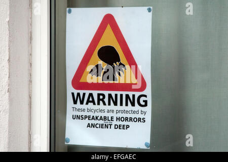 Ein Schild in einem Hausfenster, das Fahrraddiebe rät, nicht zu stehlen - Warnung. Diese Fahrräder sind durch UNSÄGLICHE SCHRECKEN aus der URALTEN TIEFE geschützt - Stockfoto