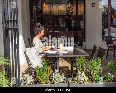 Eine Seitenansicht einer jungen spanischen Frau studieren mit ihrem Computer am Cafétisch für draußen in Santa Barbara, Kalifornien. Stockfoto