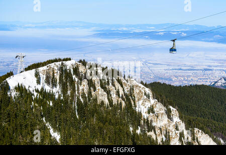 Postavaru Berg, Rumänien. Winterlandschaft mit Seilbahn von Poiana Brasov, Postavaru mit Brasov Stadtbild im Hintergrund. Stockfoto