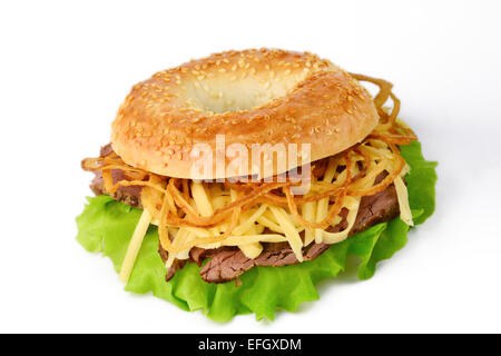 Studio isoliert: frische Sesam Bagel mit Salat, gebratenes Rindfleisch, geriebenen Cheddar-Käse und Zwiebel Ringe Stockfoto