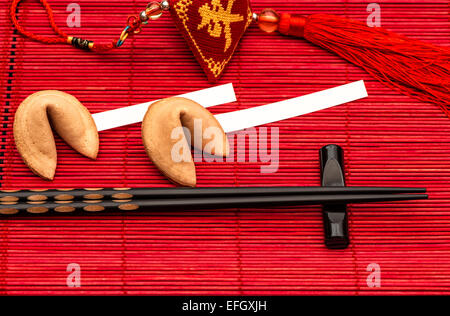 Chinesische Neujahr Glücksbringer, Glückskekse und schwarzen Stäbchen auf roten Bambusmatte Stockfoto