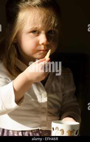 Zwei Jahre altes Mädchen Keks im Becher Tee Eintunken. Stockfoto