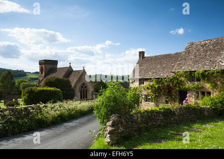 Stein-Cottages mit Rosen um die Tür neben St. Barnabas Church in Snowshill, Cotswolds, Gloucestershire, England. Stockfoto