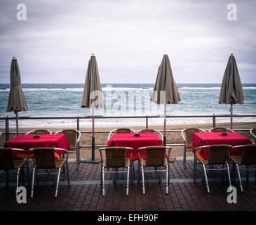 Leere Tische und Stühle im freien Restaurant mit Blick auf Strand. Stockfoto