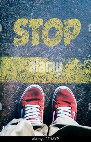 Mans Beine hinter die gelbe Linie von oben mit Stop-Schild Stockfoto