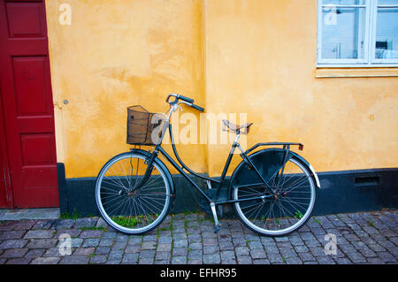 Eine einzigartige Bike mit einem Korb ruht eine leuchtend gelbe Wand illustrieren Kopenhagen Dänemark romantische Fahrradkultur. Stockfoto