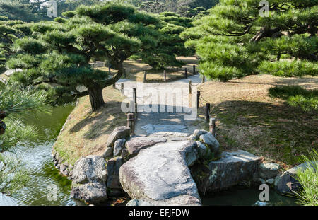Ritsurin-Koen Garten, Takamatsu, Japan. Eine steinerne Brücke zwischen schwarzen Kiefern in Byobu-Matsu Form beschnitten Stockfoto