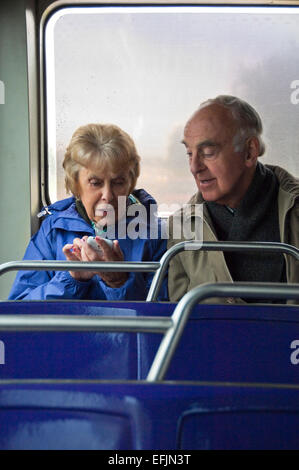 Vertikale Porträt eines älteren Paares sitzen zusammen in einem Bus mit einem Smartphone. Stockfoto