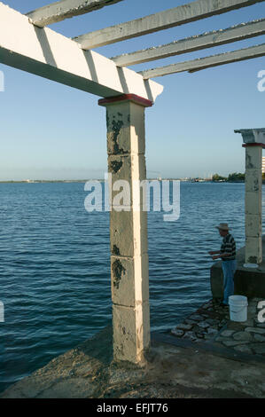 Kubanische Mann Angeln vom Ufer stehen neben einer Laube entlang Cienfuegos Bay, Punta Gorda Gegend von Cienfuegos, Kuba. Stockfoto