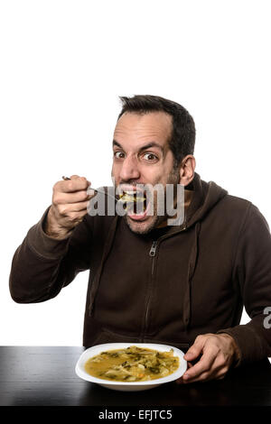 Junger Mann Essen Gemüsesuppe mit weit geöffnetem Mund Stockfoto