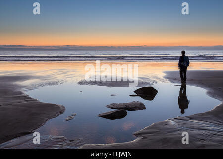 Person, die am Strand bei Sonnenuntergang, Dunraven, Wales, UK Stockfoto