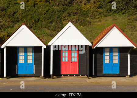 Drei bunte Strandhütten mit blauen und roten Türen in einem traditionellen englischen Zeilenstruktur und Unterschlupf gefunden am Meer Stockfoto