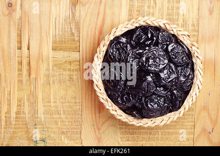 Getrocknete Pflaumen in Wicker Schüssel und auf hölzernen Hintergrund. Ansicht von oben Stockfoto